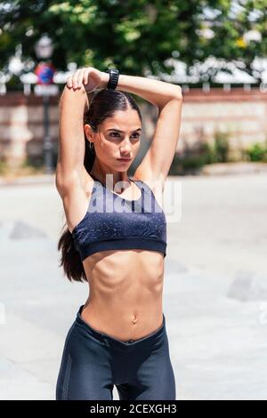 Brassière de sport et leggings confortables trottoir et bras étirant tout en s'échauffant avant l'entraînement et vue sur l'extérieur Banque D'Images