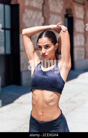 Brassière de sport et leggings confortables trottoir et bras étirant tout en s'échauffant avant l'entraînement et vue sur l'extérieur Banque D'Images