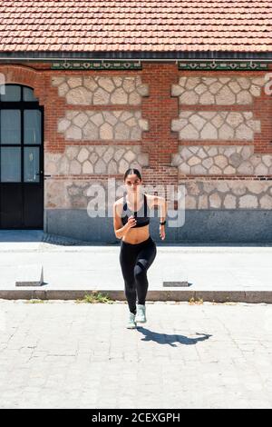 Pour une femme, courez rapidement le long de la chaussée pendant l'entraînement le jour ensoleillé en ville Banque D'Images