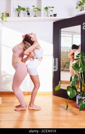 Vue latérale des femmes dans les vêtements de sport debout dos à dos À Utkatasana et en tenant les mains tout en pratiquant le yoga ensemble Banque D'Images