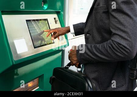 Vue rognée sur le côté d'un homme d'affaires afro-américain méconnaissable en protection Masque avec valise à l'aide du terminal de guichet automatique de la rue dans la ville de Barcelone Banque D'Images