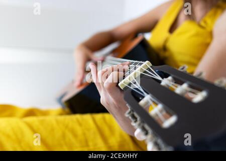 Vue latérale d'une petite femme de talent non reconnaissable assise sur le lit jouer de la guitare Banque D'Images