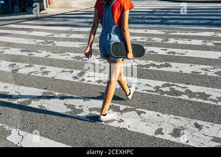 Vue arrière de crop anonyme femme millénaire avec patinage à travers route par jour ensoleillé en ville Banque D'Images