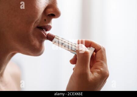 Vue latérale gros plan de la récolte femelle non reconnaissable appliquant de couleur naturelle rouge à lèvres pendant la routine de beauté du matin Banque D'Images