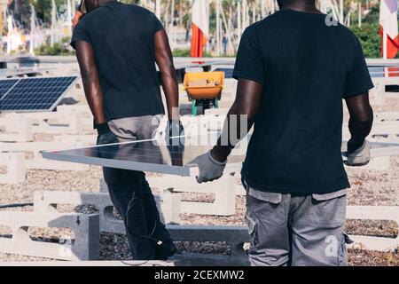 Vue arrière de la récolte des travailleurs africains américains marchant avec le solaire panneau le jour ensoleillé dans la zone industrielle Banque D'Images