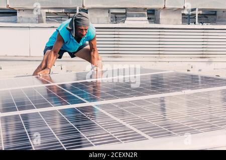 Homme sérieux installant des panneaux solaires modernes tout en travaillant dans zone industrielle de l'usine le jour ensoleillé Banque D'Images