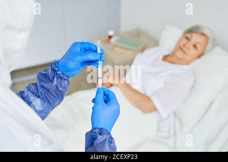 Injection sur l'épaule d'un médecin portant des gants en latex et remplissant la seringue de médicament pour patient âgé Banque D'Images