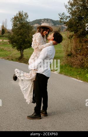 Vue latérale complète de couple amoureux récemment marié des vêtements élégants se tenant sur la route et profitant de moments romantiques ensemble pendant le voyage dans la campagne Banque D'Images