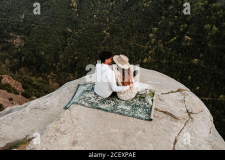 D'en haut de l'arrière vue de jeune homme et femme nouvellement mariés dans des vêtements élégants assis au sommet de la falaise rocheuse de Morro de Labella et embrassant doucement Banque D'Images