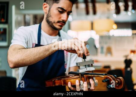 Collier en métal réglable luthier professionnel concentré sur le cou de violon pendant la restauration de l'instrument en atelier Banque D'Images