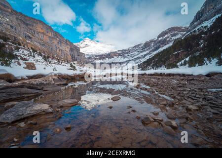 Paysage pittoresque d'une chaîne de montagnes majestueuse avec des sommets enneigés et forêt sombre avec rivière peu profonde qui coule dans la vallée Banque D'Images