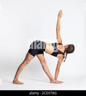 Vue latérale complète de la jeune femme pieds nus dans des vêtements de sport Exécution de la posture de yoga en triangle avec révolution sur fond blanc Banque D'Images