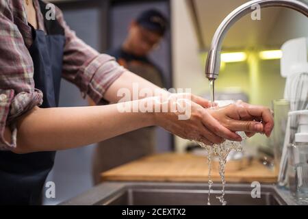 Vue de côté courte de femme se lavant les mains dans l'évier tout en ayant la boulangerie maison avec l'homme Banque D'Images