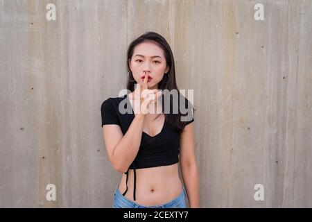 Femme asiatique calme debout avec l'index sur les lèvres et faire la démonstration de l'affiche en regardant l'appareil photo Banque D'Images