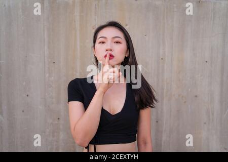 Femme asiatique calme debout avec l'index sur les lèvres et faire la démonstration de l'affiche en regardant l'appareil photo Banque D'Images