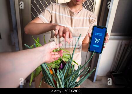 femme méconnue avec smartphone avec application mobile pour les achats en ligne prendre des provisions fraîches de liveur Banque D'Images