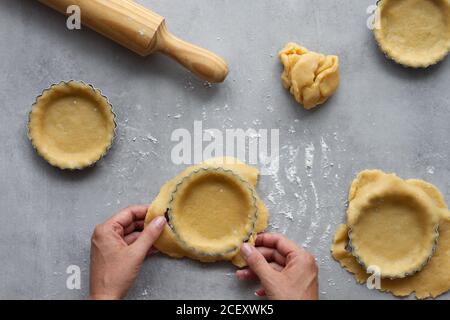 Vue de dessus de la récolte anonyme femme au foyer remplissant des formes métalliques avec pâte sablée tout en préparant la tarte au citron dans la cuisine Banque D'Images