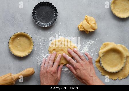 Vue de dessus de la récolte anonyme femme au foyer remplissant des formes métalliques avec pâte sablée tout en préparant la tarte au citron dans la cuisine Banque D'Images