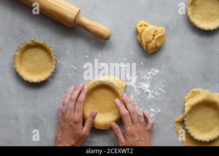 Vue de dessus de la récolte anonyme femme au foyer remplissant des formes métalliques avec pâte sablée tout en préparant la tarte au citron dans la cuisine Banque D'Images