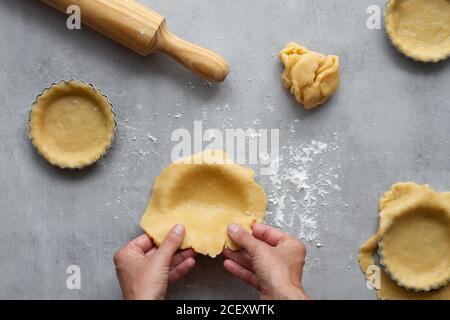 Vue de dessus de la récolte anonyme femme au foyer remplissant des formes métalliques avec pâte sablée tout en préparant la tarte au citron dans la cuisine Banque D'Images