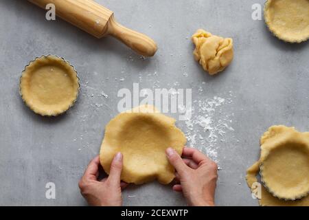 Vue de dessus de la récolte anonyme femme au foyer remplissant des formes métalliques avec pâte sablée tout en préparant la tarte au citron dans la cuisine Banque D'Images