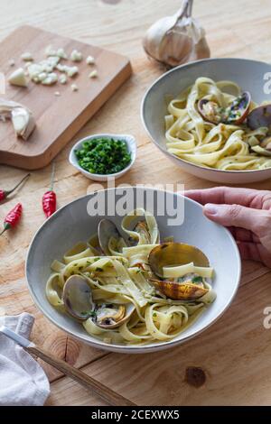 Grand angle de chef anonyme avec bol de fraîchement cuit spaghetti aux palourdes placées sur une table en bois dans le café Banque D'Images