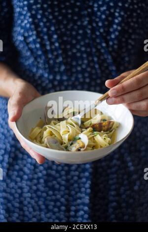 Femelle non reconnaissable debout avec bol de Tagliatelle alle Vongole et savourez un délicieux plat Banque D'Images