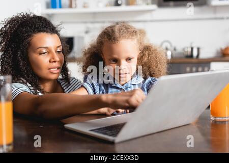 attention sélective à une femme afro-américaine pointant vers un ordinateur portable près de chez elle fille concentrée Banque D'Images