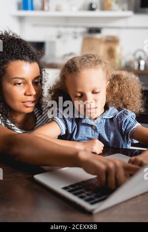 attention sélective à une femme afro-américaine pointant vers un ordinateur portable près de chez elle fille concentrée Banque D'Images