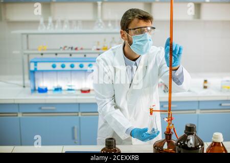 Beau chercheur en vêtements de travail de protection debout dans le laboratoire et flacon d'analyse avec liquide Banque D'Images