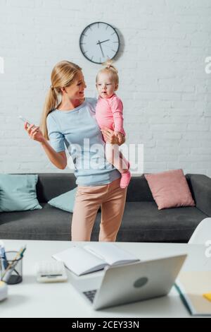 Objectif sélectif d'une femme tenant un smartphone et regardant un enfant à la maison Banque D'Images