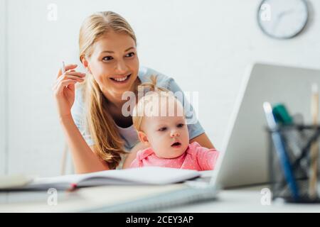 Objectif sélectif d'une femme tenant un stylo et regardant un ordinateur portable proche de l'enfant à la maison Banque D'Images