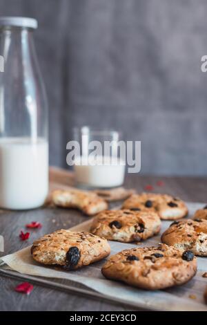 Délicieux biscuits de flocons d'avoine fraîchement cuits sur du papier de cuisson placé sur la table près de la bouteille et du verre avec du lait pendant le petit déjeuner Banque D'Images