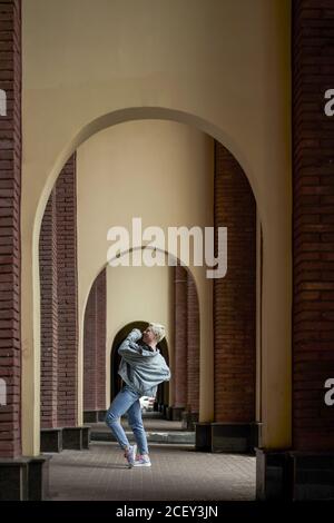 Danseuse talentueuse de vêtements en denim se exécutant dans une allée voûtée en ville et en plein air Banque D'Images