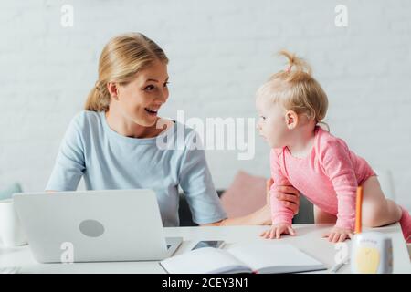 Attention sélective de la femme regardant la fille tout en travaillant avec ordinateur portable près de l'écoute-bébé sur la table Banque D'Images