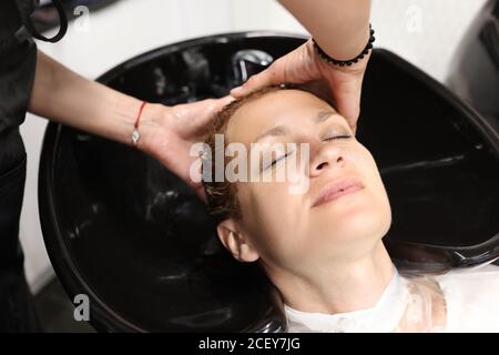 Le maître lave la tête de la femme dans le lavabo du coiffeur. Banque D'Images