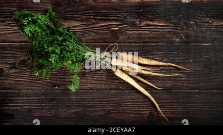Bouquet de racines de panais avec des feuilles vertes sur un panneau rustique en bois sombre, vue d'en haut Banque D'Images