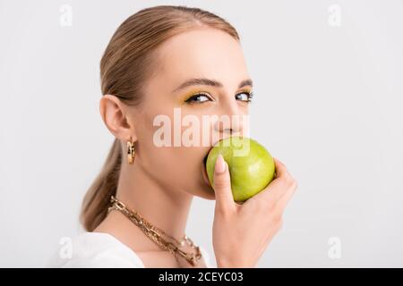 une femme blonde piquant une pomme verte et regardant un appareil photo isolé sur blanc Banque D'Images