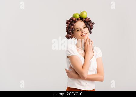 femme blonde rustique posant avec des raisins et des pommes sur la tête isolé sur blanc Banque D'Images
