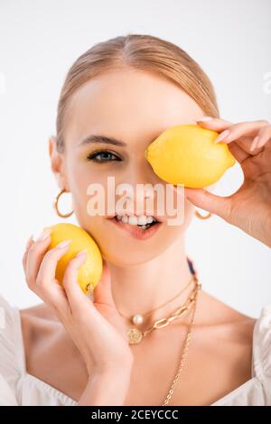 élégante femme blonde posant avec des citrons et mordant lèvre isolée sur blanc Banque D'Images