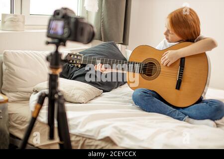 portrait d'enfant doux fille blogger étudiant des accords en guitare acoustique, elle s'assoit à la maison, aimez jouer de la guitare. auto-enseigné blogger fille enregistrer vidéo Banque D'Images