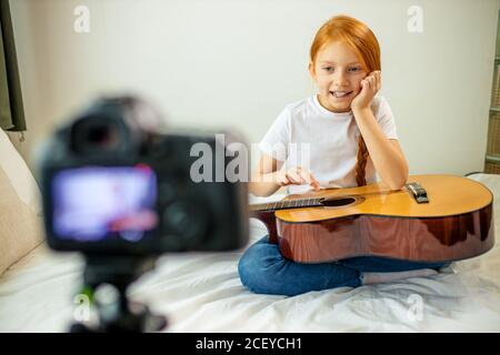 mignon adorable enfant blogueur jouer de la guitare, parler à la caméra comment elle a appris à jouer de la guitare acoustique, elle est autodidacte Banque D'Images