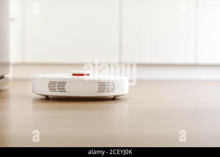 Aspirateur robot blanc sur sol stratifié, poussière de nettoyage à l'intérieur du salon. Technologie d'entretien électronique intelligente. Maison intelligente Banque D'Images