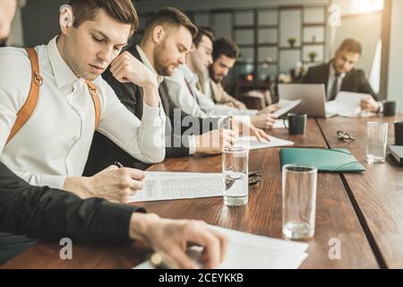 les jeunes gens d'affaires du tux s'assoient au bureau, font des notes, enregistrent des dossiers, utilisent des documents. discutent et écrivent des idées d'affaires Banque D'Images