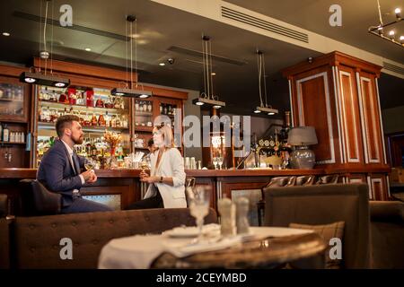 Gros plan de couple charmant en train de boire un délicieux vin au comptoir du bar dans un restaurant agréable, parlant gentiment, belle jeune femme à l'écoute de l'entreprise Banque D'Images