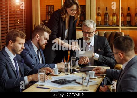 Un charmant secrétaire dans un procès strict a apporté des documents à la tête de personnes âgées pour la signature. Les meilleurs responsables attendent le début de la réunion d'affaires Banque D'Images