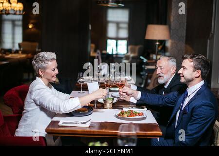 Des partenaires d'affaires heureux levant les mains avec des verres de vin, heureux de se féliciter mutuellement avec succès, posant dans le restaurant de luxe Banque D'Images