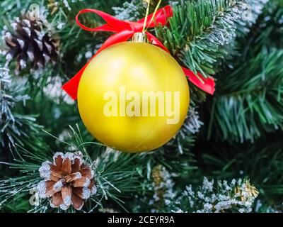 Boule de noël dorée mate suspendue à une branche de pin artificielle avec cônes réels Banque D'Images