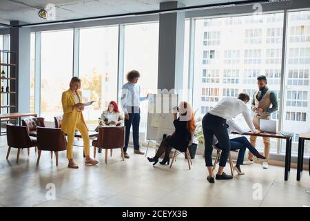 Un jeune coach caucasien confiant donne une présentation sur tableau à son équipe d'affaires ou groupe de collègues dans le bureau moderne , Teamwork conc Banque D'Images