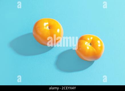 deux tomates jaunes avec de longues ombres sur fond de papier bleu Banque D'Images